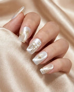 Load image into Gallery viewer, Nails with white polish and gold decorations on a beige fabric background