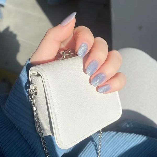 Hand holding a small white handbag with a chain detail, against a blurred background.