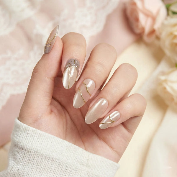 Hand with beige nail polish and gold accents against a soft pink background