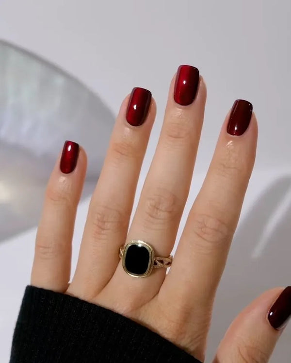 Hand with maroon nail polish wearing a gold ring with a black stone on a neutral background