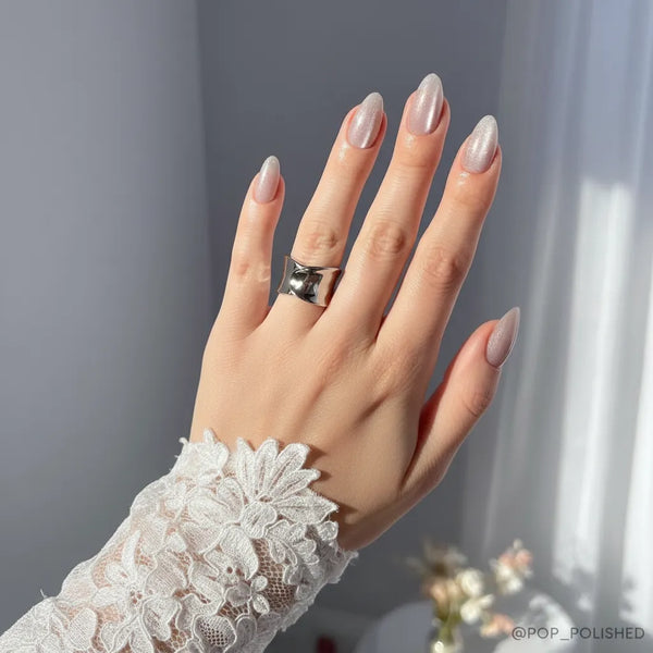 Hand with beige nail polish wearing a silver ring, against a neutral background.