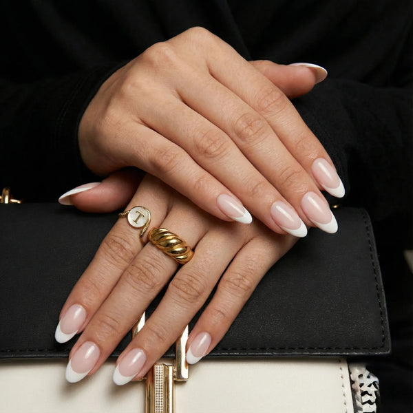 Close-up of hands with manicured nails and gold rings, holding a black handbag.