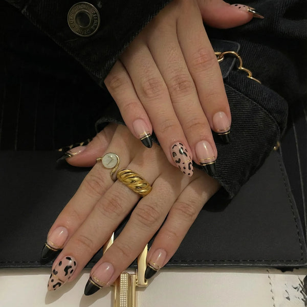 Close-up of a hand with manicured nails and rings, holding a black handbag.