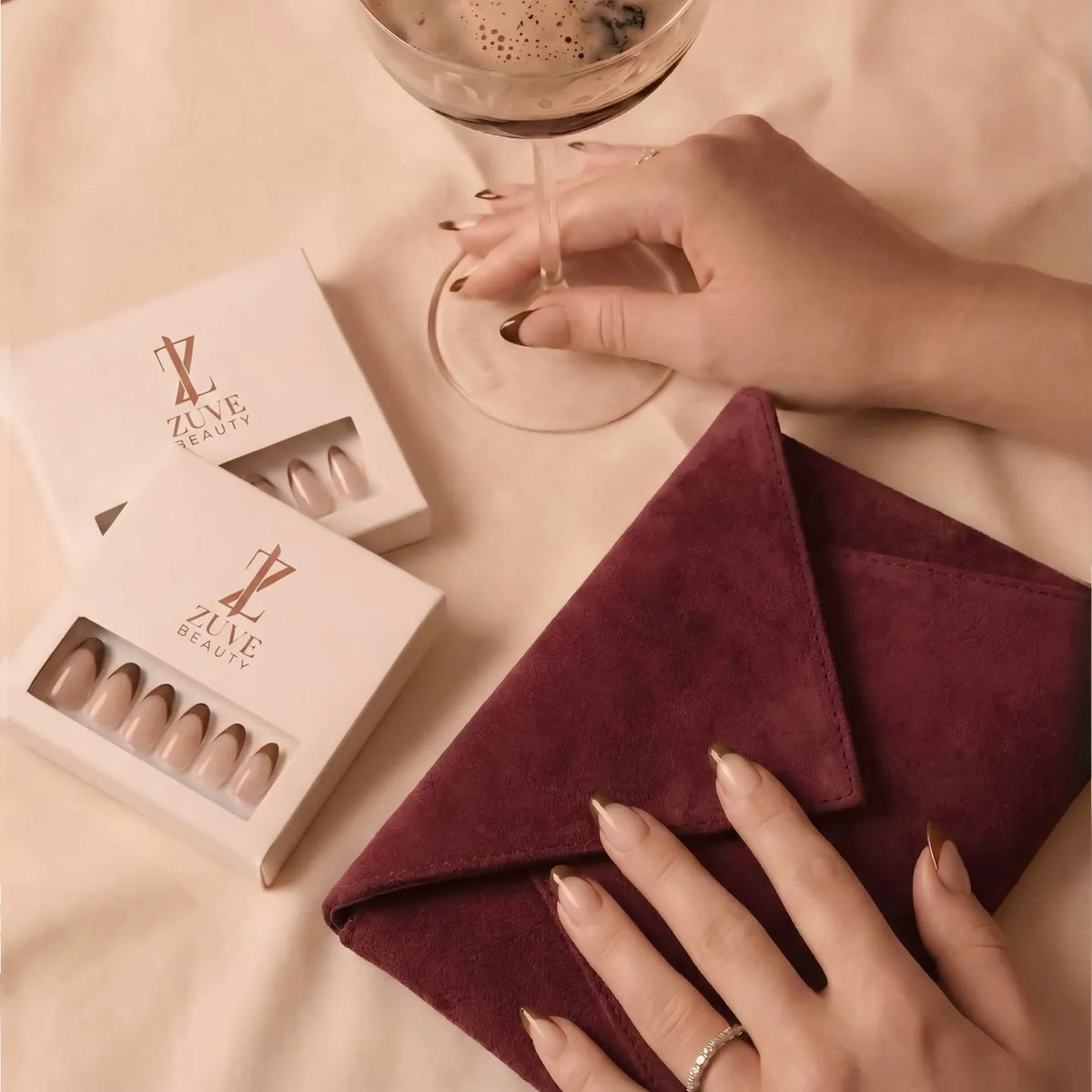 Nail art set with zu ye beauty branding, hand holding a glass of coffee, and maroon napkin on a beige surface