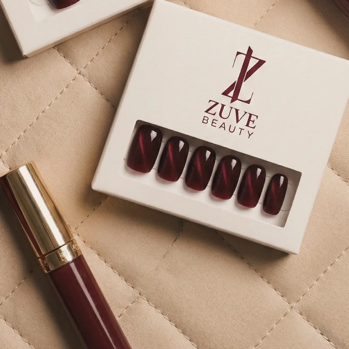 Zuve beauty nail art set with red nail tips and a gold pen on a beige quilted surface